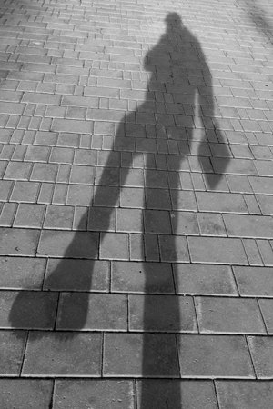 A woman's shadow is cast on a brick sidewalk. The image has a moody, mysterious feel to it, as the shadow appears to be a person rather than just an objectの写真素材