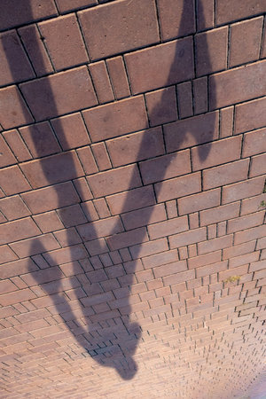 A brick wall casts a shadow of a person on the ground. The shadow is dark and elongated. The brick wall itself is a solid structureの写真素材