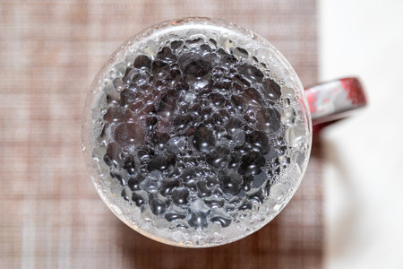 A mug filled with a dark liquid with a lot of bubbles. The bubbles are black and the liquid is clearの写真素材