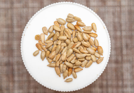 A white plate with a pile of sunflower seeds on it. The seeds are scattered all over the plate, and they are of different sizes. Concept of abundance and variety, as the seeds come in different shapesの写真素材