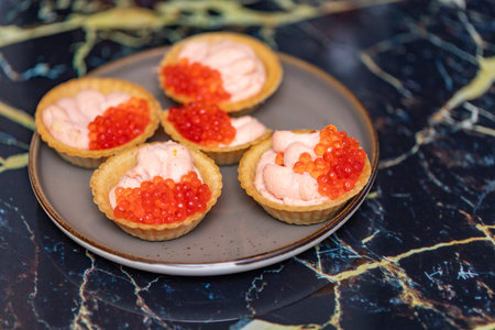 A plate of four small pastries with red caviar on top. The plate is on a marble countertopの写真素材