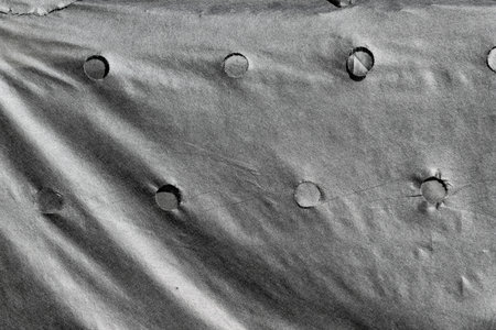 A black and white photo of a piece of cloth with holes in it. The holes are in the shape of circles and are scattered all over the clothの写真素材