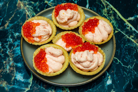 A plate of five small pastries with red berries on top. The plate is on a marble countertopの写真素材