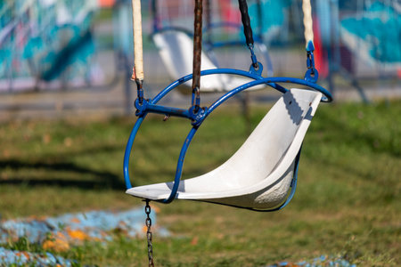 A swing with a white seat is hanging from a blue chain. The swing is emptyの写真素材