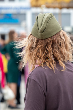 A person with a green hat and long hair is standing in front of a crowd of people. The person's hair is messy and they are wearing a green hat.の写真素材