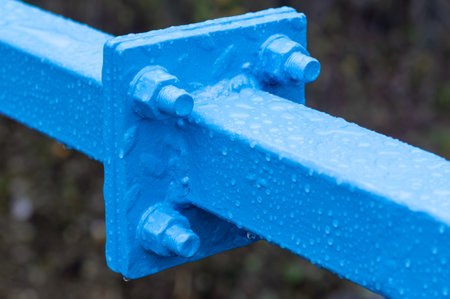 A blue metal beam with a blue bolt on it. The bolt is shiny and wet. Concept of strength and durability, as the metal beam is able to withstand the elements and remain sturdyの写真素材