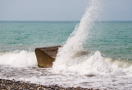 A large wave is crashing into a rock on the beach. The water is white and frothy, and the rock is partially submerged. The scene is dynamic and powerfulの写真素材