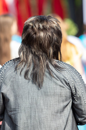 A woman with long hair is wearing a black jacket with a lot of beads. She is standing in a crowd of peopleの写真素材