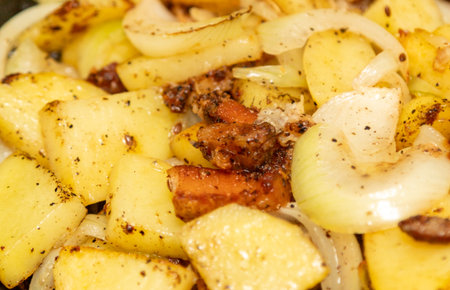 A plate of food with potatoes, onions, and bacon. The potatoes are seasoned with salt and pepperの写真素材