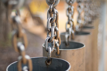A row of metal chains hang from a metal pole. The chains are attached to metal cups, which are hanging from the chain. The cups are empty and appear to be part of a decorative displayの写真素材