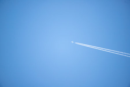 A jet is flying through the sky, leaving a trail of white smoke behind it. The sky is a bright blue,...