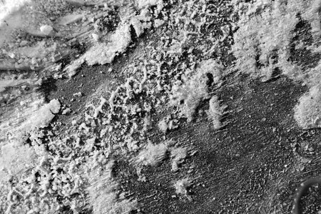 A black and white photo of a rocky surface with a lot of snow and ice. The photo has a moody and...