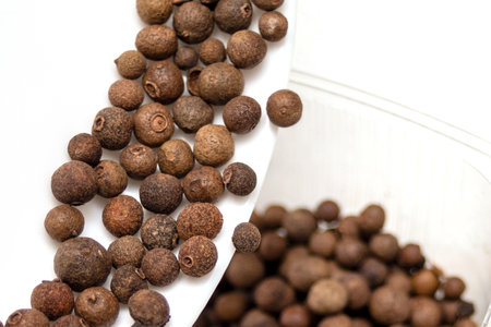 A pile of brown colored peppercorns. The peppercorns are scattered all over the white surface