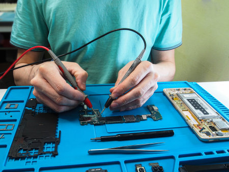 A technician is repairing a phone. Looks for a malfunction in the smartphone with a multimeter.