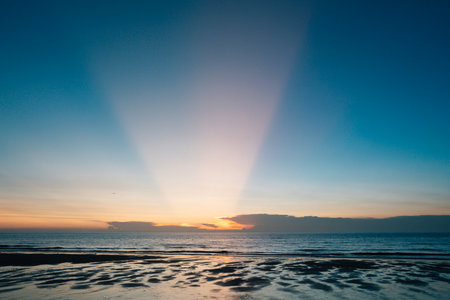Beautiful sunset on the beach with rays of light coming through the cloudsの写真素材