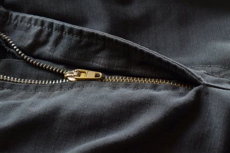 Close-up of half open gold zipper on black pants.
