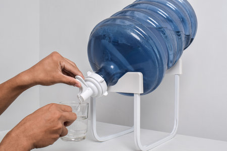 Man's hand pours water into a glass cup from a large gallon. Pouring fresh clear water from a large blue gallon into a glassの写真素材