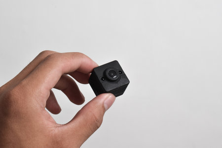 Hand holding a spy camera isolated on white background. Black security camera, Mini spy cameraの写真素材