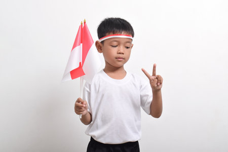 Cute little Asian boy holding Indonesian flag and posing showing two fingers in a peaceful gesture to celebrate Indonesian Independence Day on August 17 isolated on white background.の写真素材