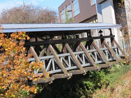 Roof covered wooden pedestrian bridge over Alzette river in Walferdange, Luxembourgの写真素材