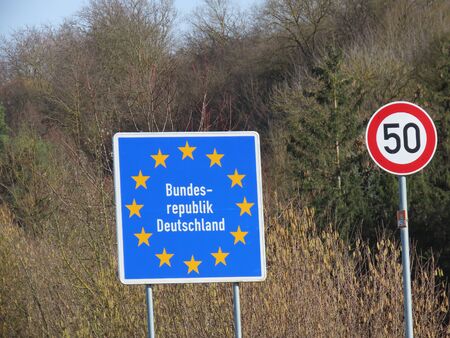 German border on small road. Blue board with yellow EU stars, Bundesrepublik Deutschland means...