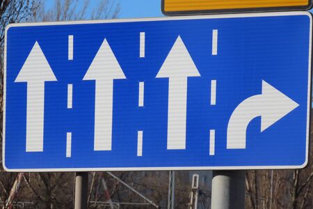 Road sign Directions of lines: rectangle blue sign with 3 white arrows straight ahead and one to the right. Early spring sunshineの写真素材