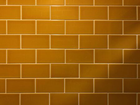 Yellow tiles on a wall in brick like pattern, uneven light from top left cornerの写真素材