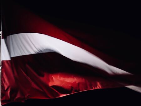Latvian flag waving in strong wind at dark night, lots of motion blur