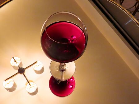 Glass of red wine on mirror surface, reflecting the wine and ceiling lamp
