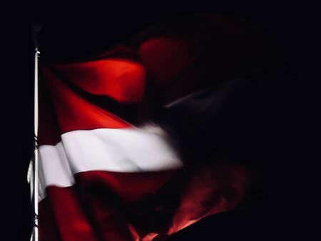 Latvian flag waving in strong wind at dark night, lots of motion blurの写真素材