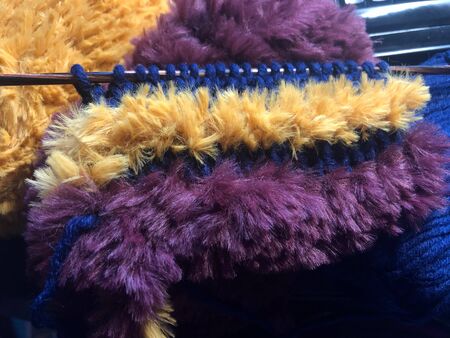 Knitting sample with stripes from yellow and dark red fluffy and dark blue flat yarn, on wooden...