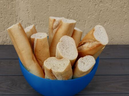 Cut pieces of French traditional baguette bread stacked in blue plastic bowl, ready to be taken and...