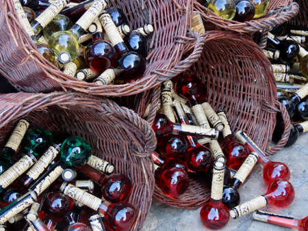 Echternach, Luxembourg - August 3, 2019. Beerenweine liquor bottles on offer in a street market, plenty of red and green bottles rolling out of wicker basketsのeditorial素材
