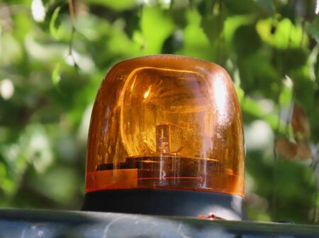 Orange flashing warning light on top of a road maintenance vehicle, close up on a sunny summer day,...