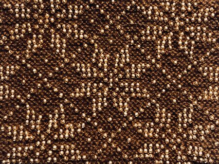 Traditional geometric ornament made of golden yellow glass beads on woven wool base, macro close upの写真素材