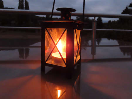 Lantern with burning tea candle in dark night on reflective surface