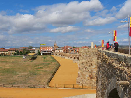 Medieval bridge over Orbigo river in Hospital de Orbigo, Leon, Spain, decorated with ancient flags for medieval festival held to remember the famous tournament of 1434. Pilgrim figures in distanceの写真素材