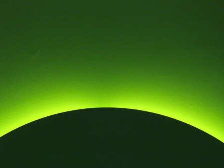 Gradient colour green light in background and part of a dark green disc or sphere in front of it. Concept of green planet rising, dawn, sunriseの写真素材