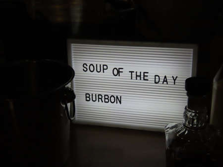Light box with words Soup of the day Burbon - also Bourbon or maybe Whiskey. Outlines of a glass bottle and drink cooling bucket in contrasting darknessの写真素材