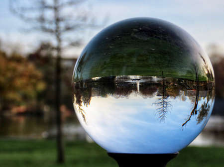 Merl park in Luxembourg in golden hour light on an autumn day - pond and water fountain, yellow trees seen through crystal ballの写真素材
