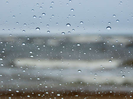 Baltic sea waves during a spring storm seen through a window with raindrops close up and bokeh...