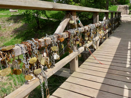 Lots of love padlocks with newlyweds names engraved chained on railings of a wooden bridge. Wedding tradition in Europe. Photo taken in Kuldiga, Latvia - May 22, 2021のeditorial素材