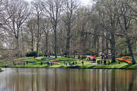 Lake water, colorful tulips in flower beds, people walking in Keukenhof gardens, Lisse, Netherlands - April 14, 2022のeditorial素材