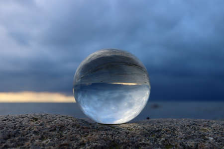 Crystal ball on the beach, sitting on a boulder, dark clouds reflecting in the ball, pending stormの写真素材