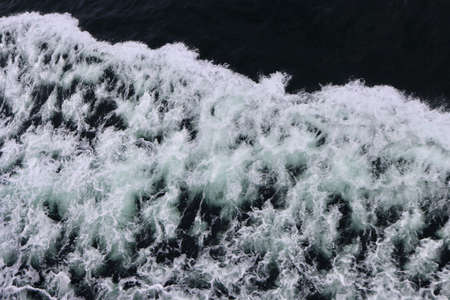 Stern waves with white foam tips on greyish blue sea water, photo taken from aboard ship. Selective...