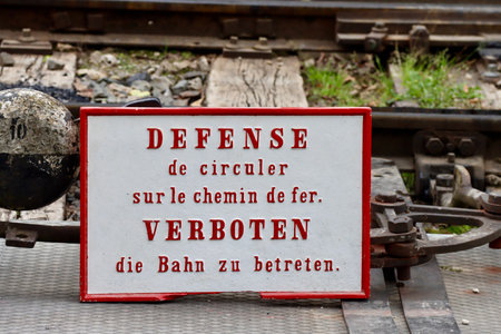 Historic safety sign on railway tracks saying in French and German FORBIDDEN walking on railway tracksの写真素材
