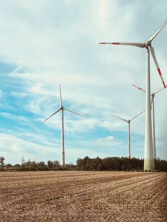 Electric wind generators standing in empty field against bright sky with clouds. Germany