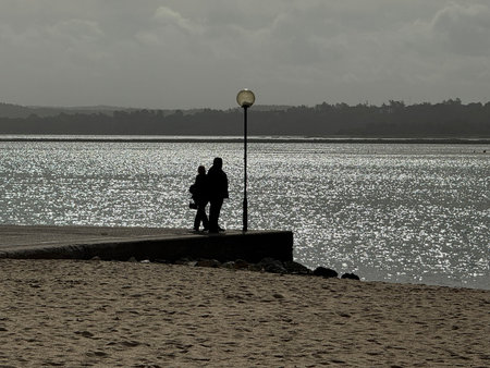 Beach view by the Obidos lagoon in Foz do Arelho, Portugal. A couple standing by the sunlit waterの写真素材