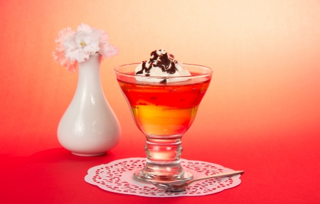 Glass with a dessert, a teaspoon, a napkin and a vase with the flowers on a pink backgroundの写真素材