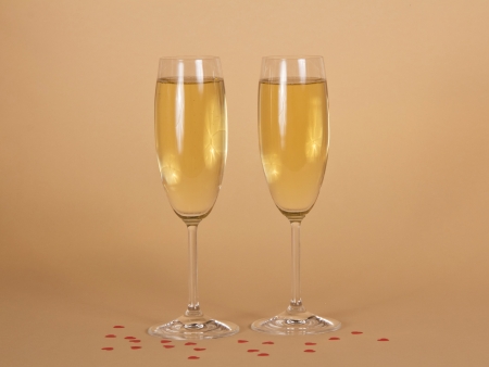 Two wine glasses of champagne and small hearts on a beige backgroundの写真素材